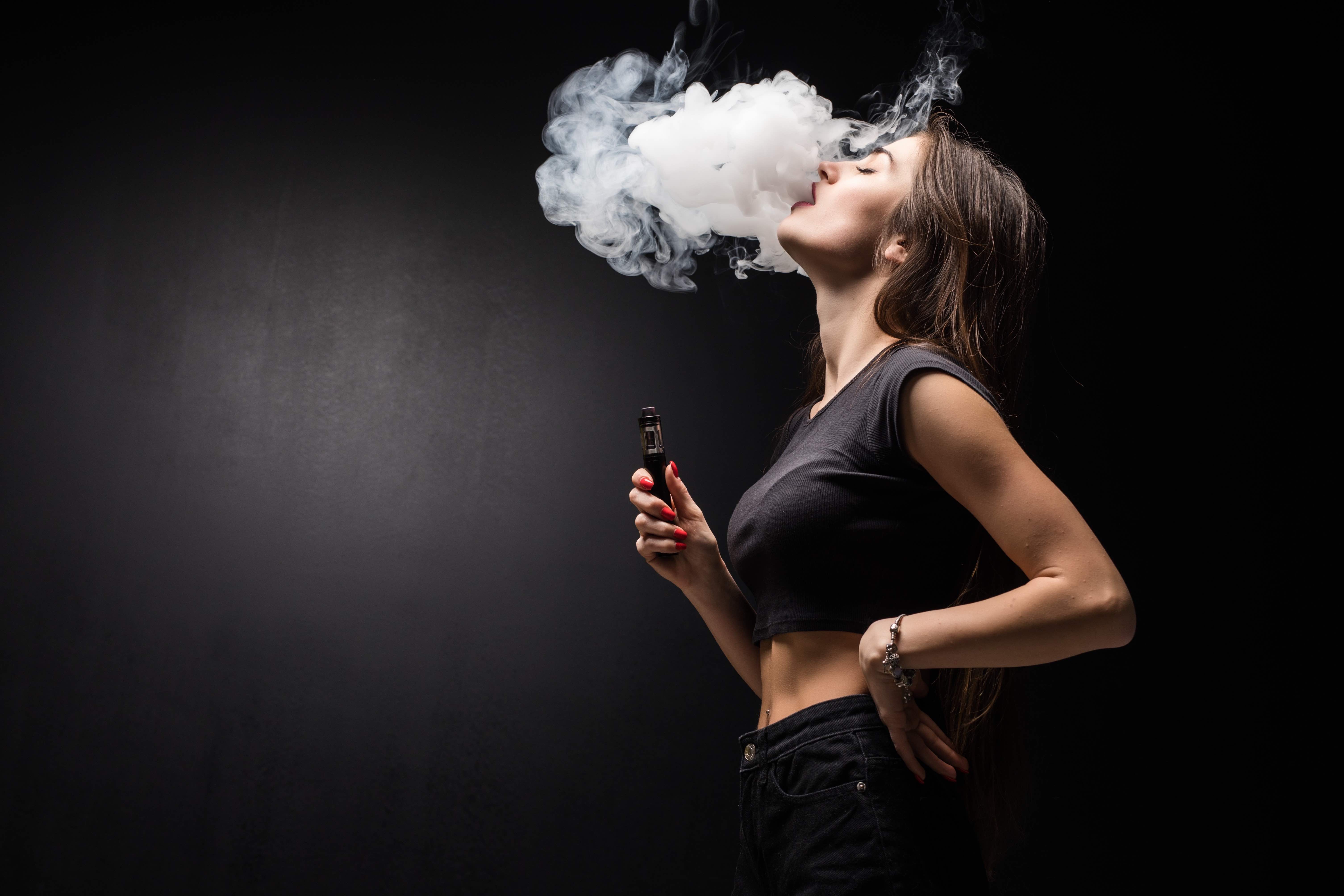 young-sexy-woman-is-vaping-smoking-e-cigarette-cloud-vapor-black-wall 